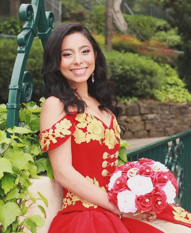 Quinceañera portrait in a red and gold charro dress with a bouquet