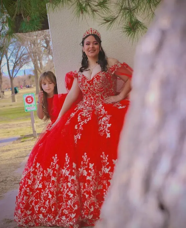 Quinceañera in a red butterfly gown posing under a pine tree