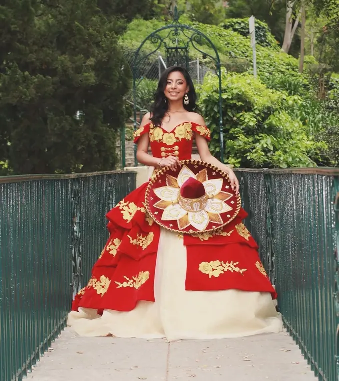 Charro-style quinceañera holding an embroidered sombrero on a bridge