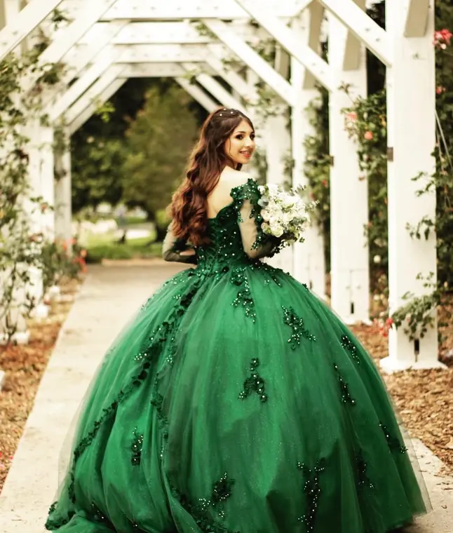 Quinceañera in an emerald green gown under a rose garden arbor