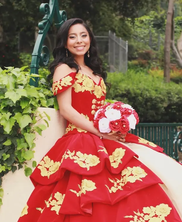 Quinceañera seated in a red velvet gown with gold floral embroidery