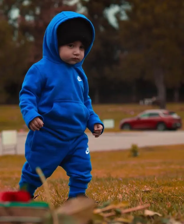 Toddler in a blue hooded tracksuit walking across an autumn park
